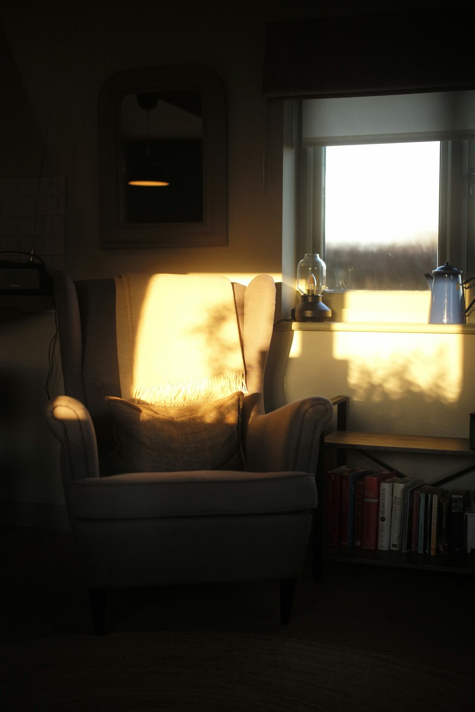 Cozy armchair with a blanket next to a bookshelf.