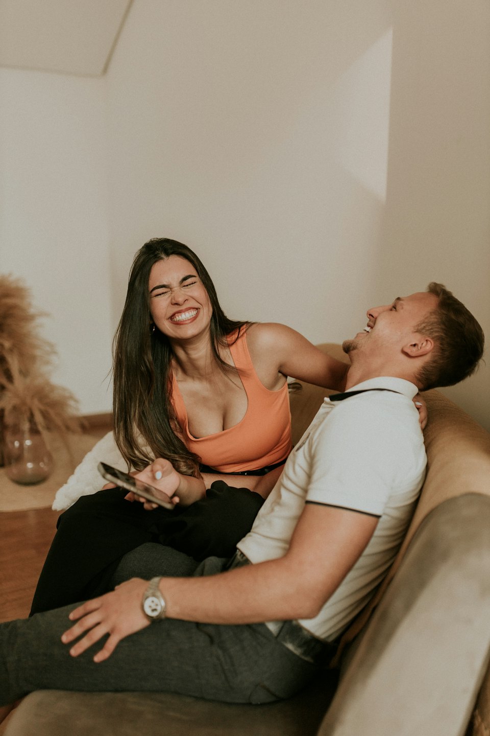 Woman laughs while holding a smartphone on a couch.