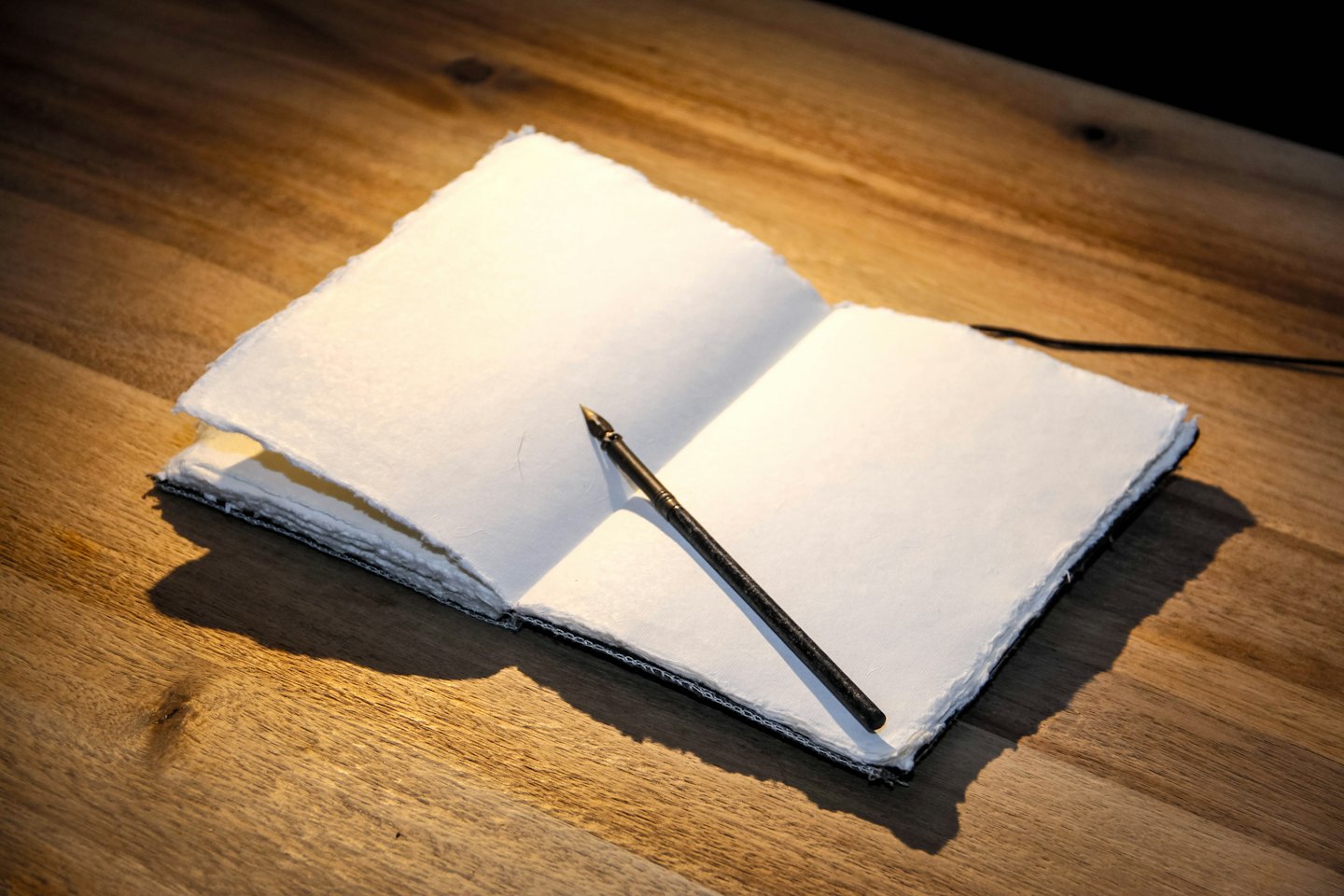 Notebook and quill pen on a wooden table.